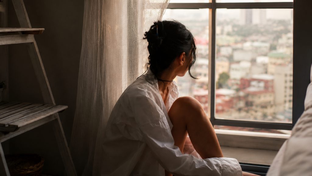 Femme assise près d’une fenêtre dans un moment de calme et d’introspection